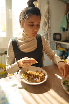 A young woman happily enjoys a delightful meal in a cozy, bright, and sunlit kitchen full of warmth and charm