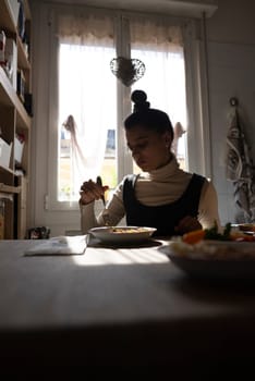 A woman finds happiness while enjoying a delightful meal in her cozy, sunlit kitchen, in a serene atmosphere