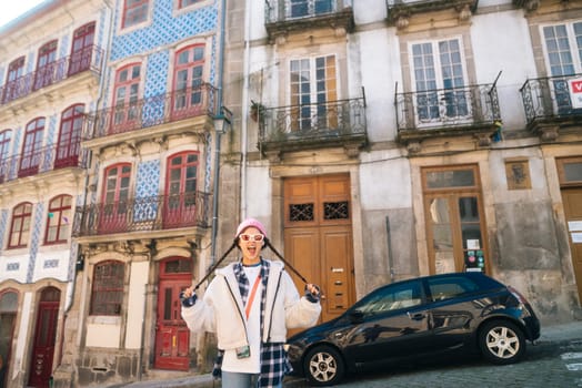 A stylish individual poses in front of vibrant buildings, showcasing modern fashion in an urban environment.