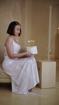 Cute young woman with short hair and white dress holding birthday cake with candles for her birthday. High quality photo