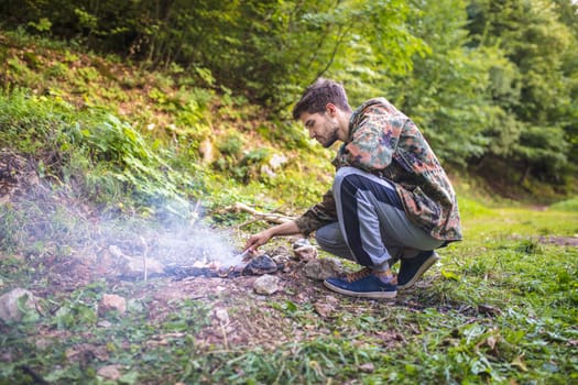 Young camper lighting a fire in the forest during his camping trip, enjoying the wilderness