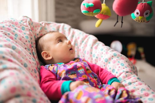 Newborn baby girl in a crib looking at colorful toys hanging above.