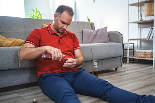 Mature man sitting on the floor and drinking alcohol.