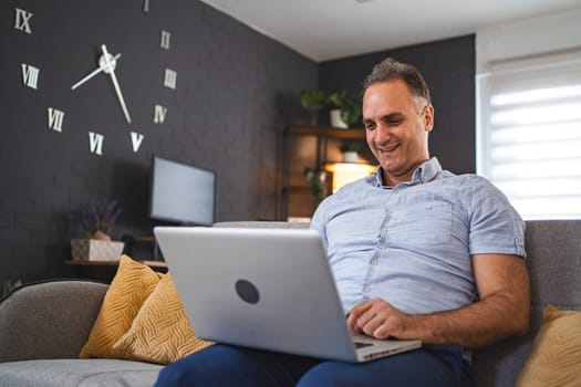 Middle aged Caucasian man using laptop on the sofa.