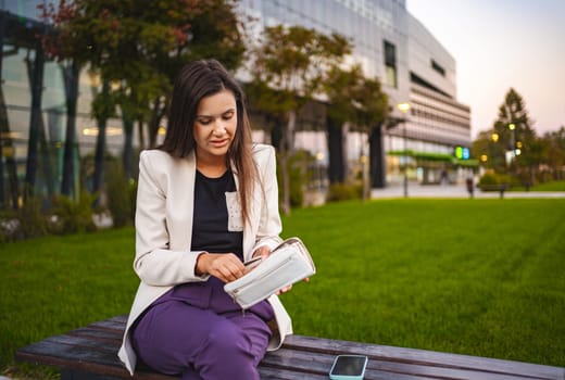 Businesswoman sitting at the park after work checking her wallet.