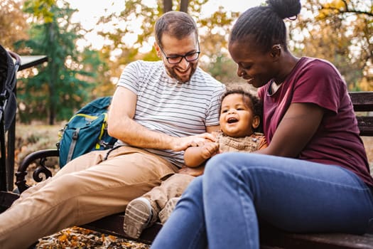Mixed race couple is sitting on a park bench with their son.