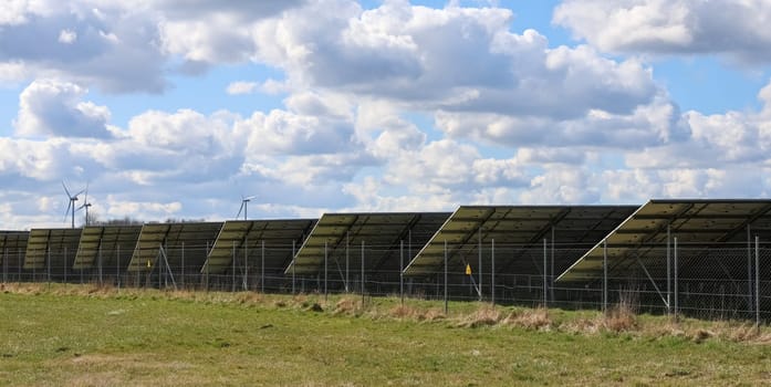 Solar panels and wind turbines are producing renewable energy in a field, contributing to a sustainable future under a cloudy sky