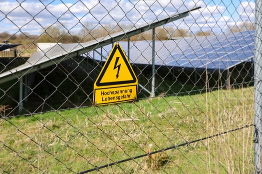 High voltage warning sign on fence protecting solar panels, representing safety and renewable energy