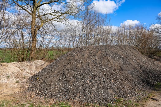 Gravel pile on a construction site with trees, bushes and a blue sky with clouds in background