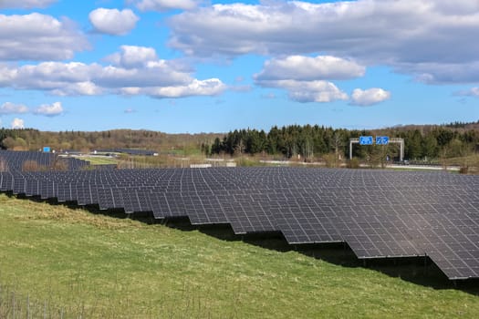 Large photovoltaic plant providing clean energy near a highway, under a cloudy sky in spring