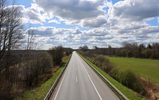 Straight asphalt road crossing a rural landscape under a partially cloudy sky on a sunny day