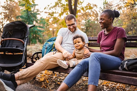 Mixed race couple is sitting on a park bench with their son.
