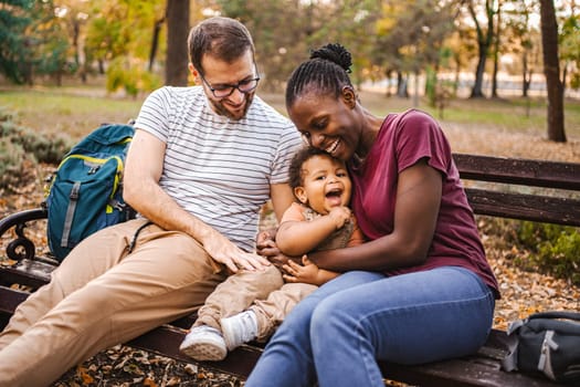 Mixed race couple is sitting on a park bench with their son.