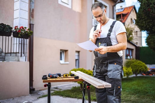 Mature male carpenter working with wooden plank outdoors.