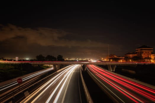 Car Light Trails on Highway Approaching and Leaving Valencia.Long exposure photograph capturing the dynamic movement of car light trails on a busy highway entering and exiting the vibrant city of Valencia. The image showcases the bustling nighttime traffic