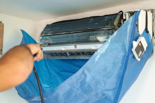 The technician are cleaning the air conditioner by spraying water.