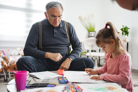 An elderly man and a young girl enjoy a creative afternoon together, drawing.