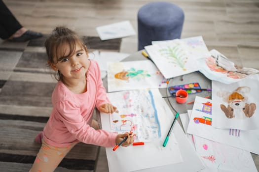 A cheerful child joyfully engages in colorful art creation on the floor.