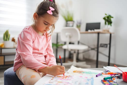 A child is deeply focused on drawing with vivid markers at her desk.