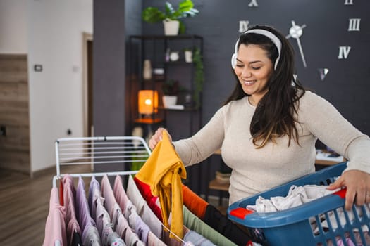 Woman listening to music while hanging the laundry on drying rack at home.