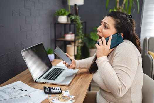 Frustrated woman talking on the phone while doing home finances.