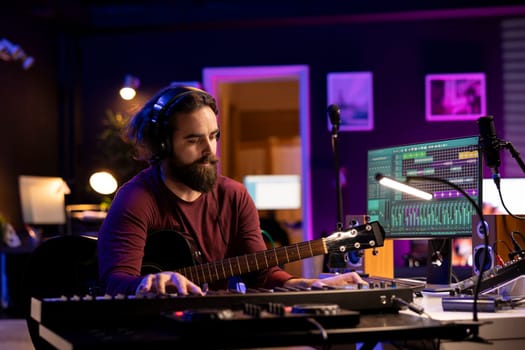 Skilled artist musician composing a song and playing his guitar, acoustical engineering techniques with daw software interface on computer. Producer creating music with instruments and audio gear.