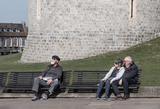 Windsor, UK - Apr 03, 2025 - Elderly people siting relax on a wooden bench in front of Windsor castle. Pensioner time and Lifestyle of retirement, use it as your Wallpaper, Poster and Space for text, Selective focus.