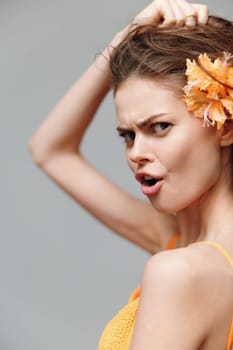 A fashionable young woman embodies summer energy with a playful expression, vibrant orange flower, and soft gray backdrop, ideal for fashion and emotional imagery.