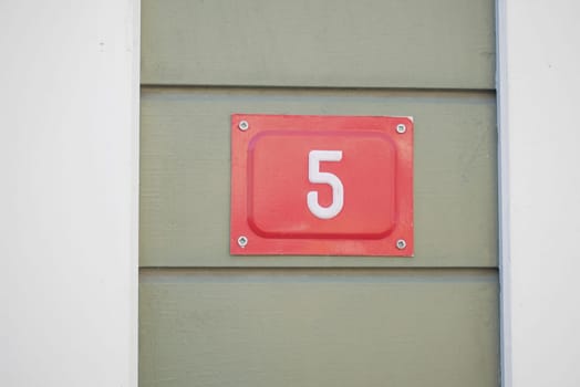 Bright red number five displayed on a green wall during the day