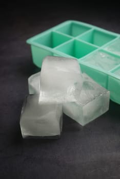 Three clear ice cubes are resting next to a mint green ice tray.