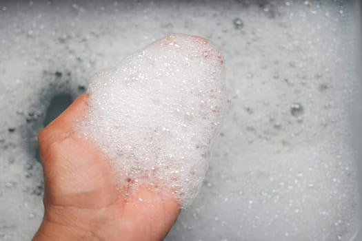 Soapy bubbles accumulate on a hand in warm, running water.