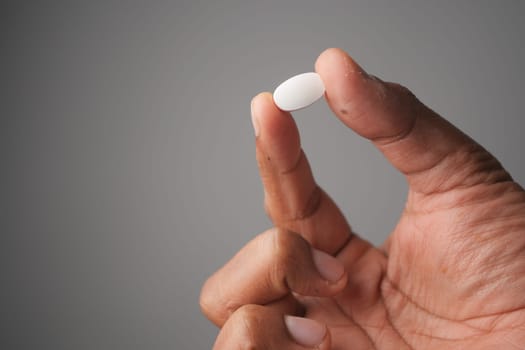 A hand is holding a small white pill against a plain background.