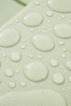 Water beads form a pattern on a green background, reflecting soft light.