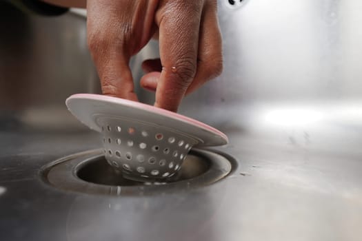 Hand is inserting a sink strainer into a drain to prevent clogging.