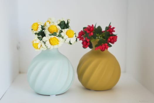 Two decorative vases hold vibrant flowers on a minimalist shelf.