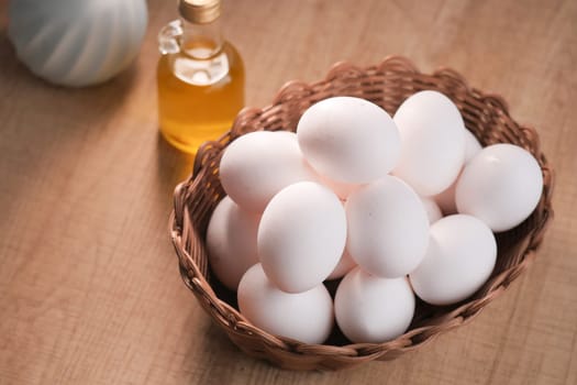 A woven basket holds a dozen white eggs beside a bottle of cooking oil.