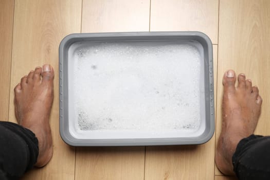 Bare feet soak in a bubbling container on wooden floor at home.