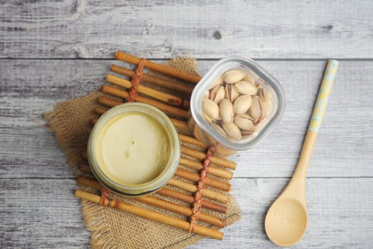 Nut spread sits next to pistachios and a spoon on a rustic surface.