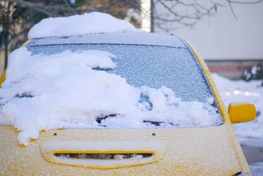 A yellow car is blanketed in fresh snow on a chilly winter day.