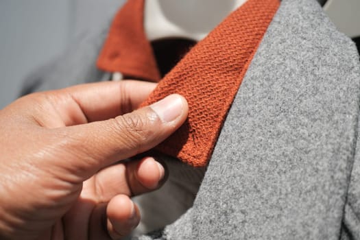A hand is inspecting the collar of a gray coat featuring a rust-colored detail.