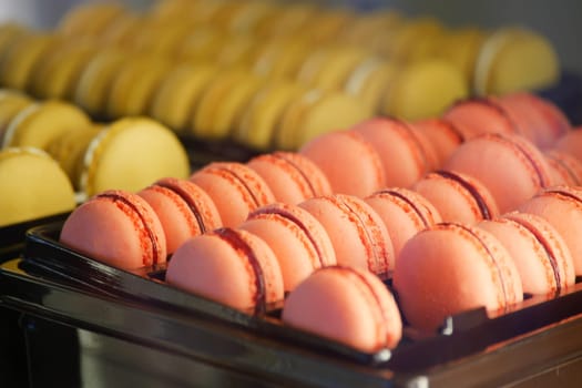 Rows of pink and yellow macarons attract customers in a bakery.