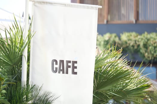 A sign displaying the word cafe is surrounded by lush green plants.