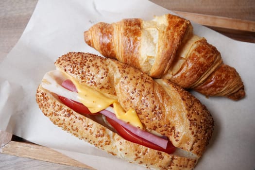 Delicious croissant and sandwich with ham, cheese, and tomato on a tray.