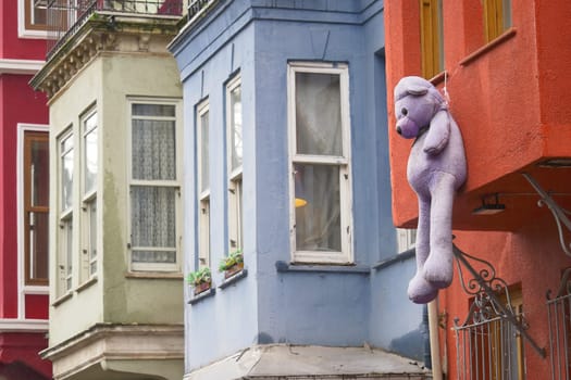 A large purple teddy bear hangs from a vibrant building in a city.