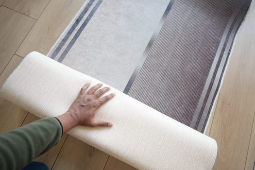 Person is unrolling a soft rug in a cozy living space to enhance decor.