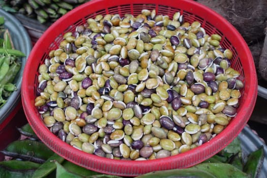 Freshly harvested beans in various colors fill a woven basket at a market.