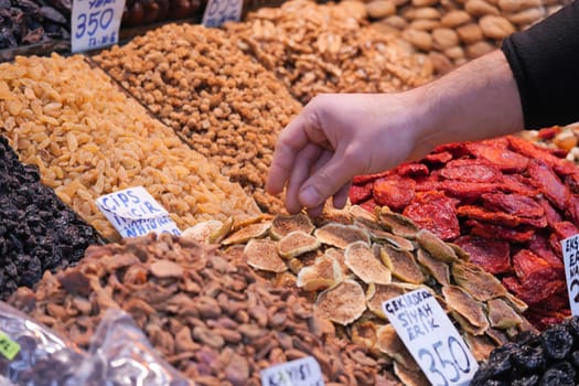 A person is selecting dried fruits and nuts at an outdoor market.