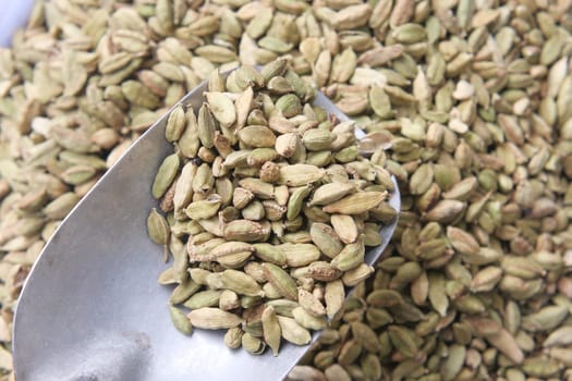 Green cardamom pods are shown in a metal scoop at a spice market.