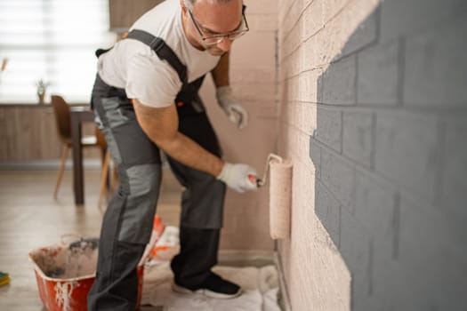 A man is seen in the midst of painting a wall using a paint roller. The wall appears to be getting a fresh coat of paint as the man carefully applies the roller in steady strokes.