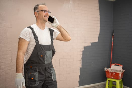 A man wearing overalls is engaged in a phone conversation on his cell phone. He appears focused as he communicates, standing in an outdoor setting.